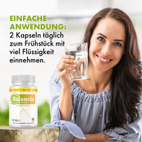 Thumbnail for Frau hält Glas Wasser neben Balancio Premium Dose mit Anwendungshinweis 2 Kapseln täglich