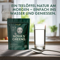 Thumbnail for Standbeutel Nova’s Greens neben Glas Wasser und Löffel auf Tisch vor hellem Hintergrund mit Pflanzen